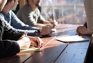 people sitting on chair in front of table while holding pens during daytime