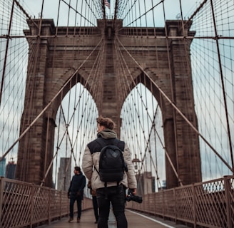 man in black jacket and black pants standing on brown bridge