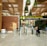 A modern airport terminal with an 'International departures' sign displayed prominently in multiple languages. The architectural design features a high ceiling with decorative plants hanging from above and polished stone flooring. Security personnel and travelers are visible near the entrance gates, and there is a blend of natural and artificial lighting.
